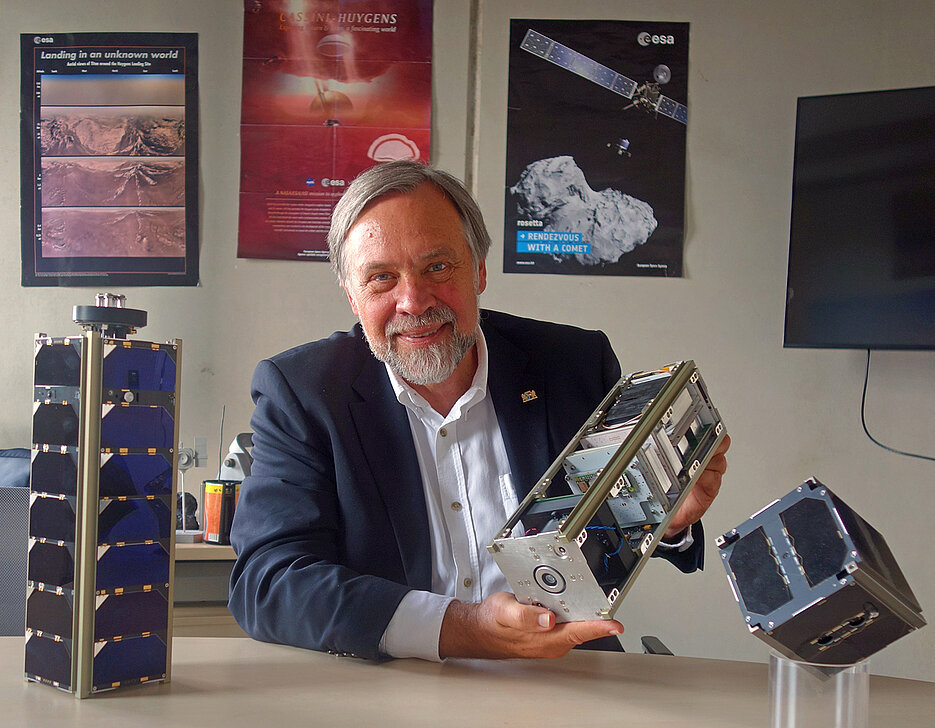 Klaus Schilling mit den Satelliten, die sein Berufsleben geprägt haben. UWE und NetSat im Vordergrund; auf den Postern im Hintergrund HUYGENS und ROSETTA, die er während seiner Tätigkeit in der Industrie mit realisieren half.