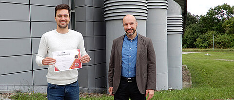 Der preisgekrönte Informatiker Martin Sträßer und Professor Samuel Kounev mit der Urkunde, die es für die herausragende Masterarbeit gab.