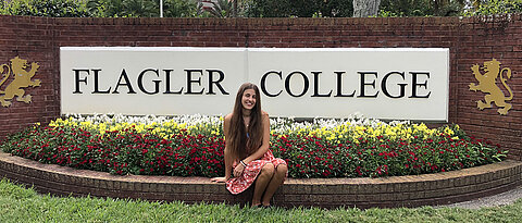 Mona vor dem Logo des Flagler College.